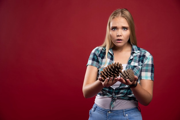 Free photo blonde woman holds oak tree cone in the hand and gives surprized poses.