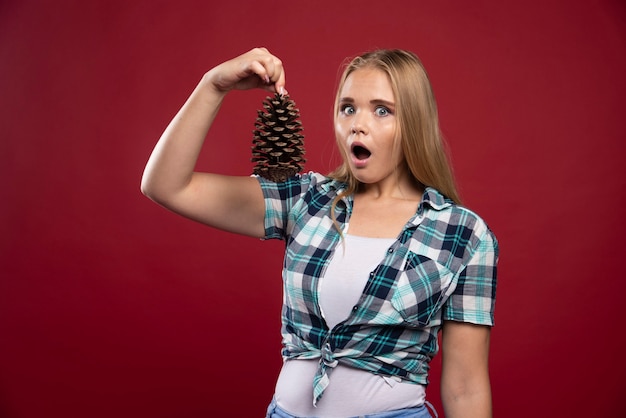 Blonde woman holds oak tree cone in the hand and gives surprized poses.