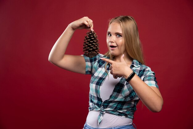 Free photo blonde woman holds oak tree cone in the hand and gives surprized poses.