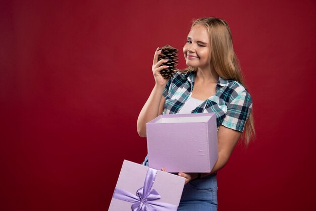 Blonde woman holds oak tree cone in the hand and looks positive and joyful.