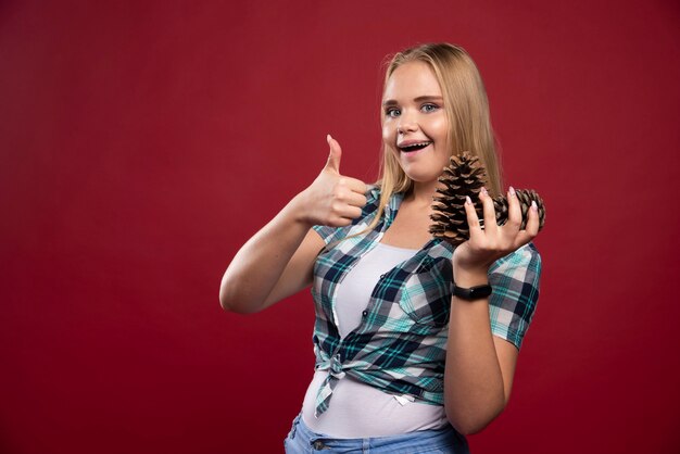 Blonde woman holds oak tree cone in the hand and looks positive and joyful.