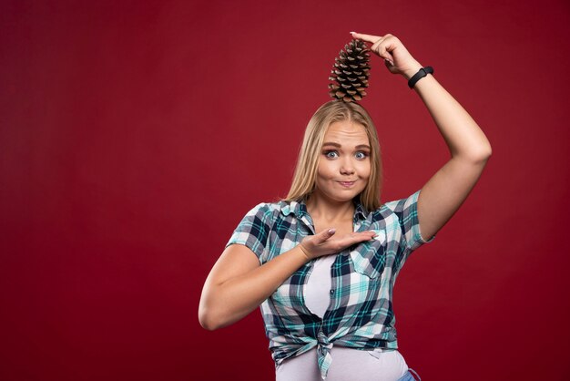 Blonde woman holds oak tree cone at her head and feels positive.