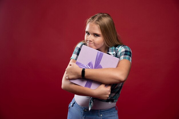 Blonde woman holds tight a gift box and gets jealous about sharing.