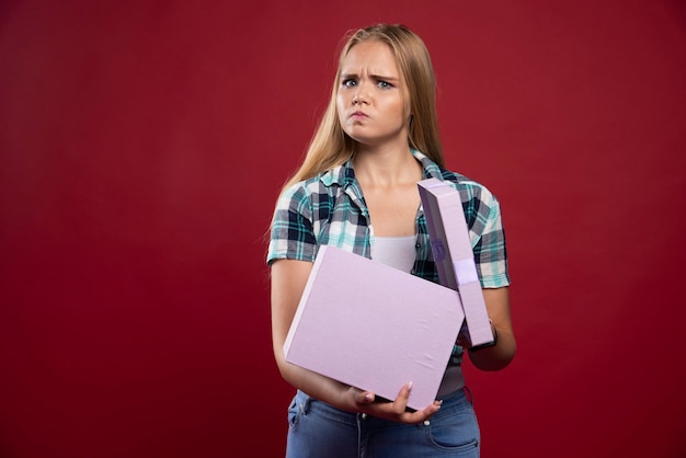 La donna bionda tiene stretta una confezione regalo e sembra confusa e insoddisfatta.