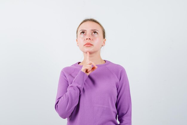 The blonde woman is thinking by holding her forefinger under chin on white background