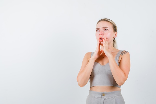 The blonde woman is thinking by holding her hands around mouth on white background