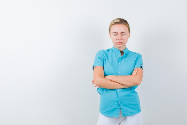 Blonde woman keeping arms folded, shutting eyes in blue blouse isolated