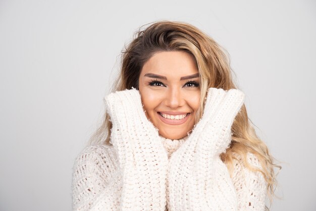Блондинка женщина в вязаном свитере счастливо улыбается.