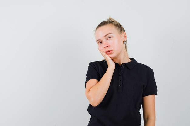 黒のTシャツで彼女の手のひらに頬を傾けているブロンドの女性