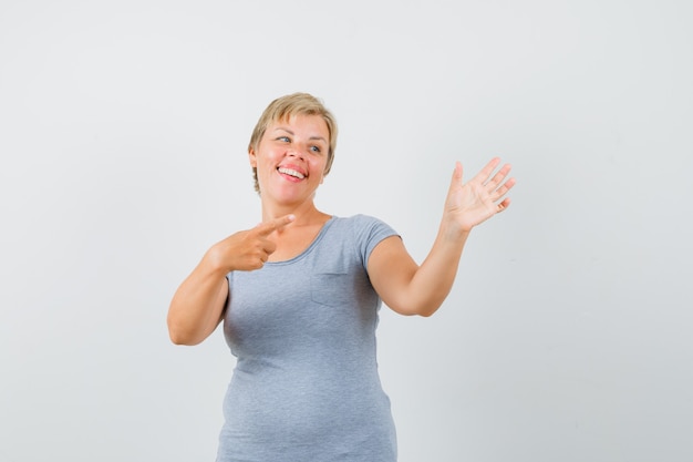 Blonde woman in light blue t-shirt pointing to her hand and looking cheerful , front view.