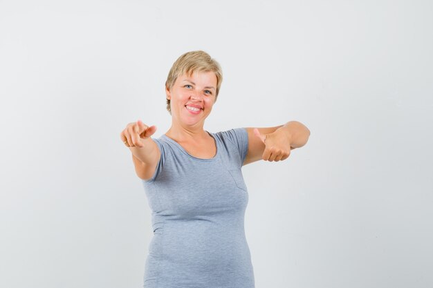 Blonde woman in light blue t-shirt pointing at herself and looking happy , front view.