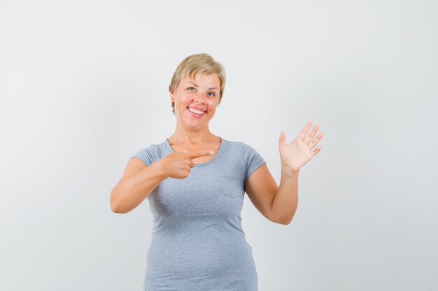 Blonde woman in light blue t-shirt pointing to the right side and looking cheerful , front view.