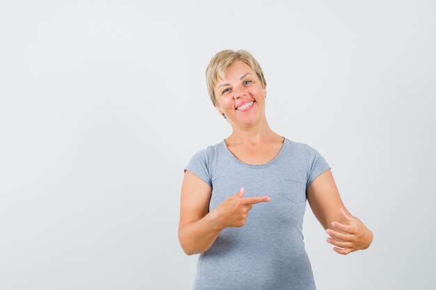 Free photo blonde woman in light blue t-shirt pretending like reading news on phone and smiling and looking cheerful , front view.