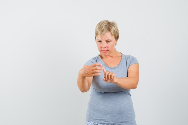 Blonde woman in light blue t-shirt pretending like to zoom something on phone and looking focused , front view.