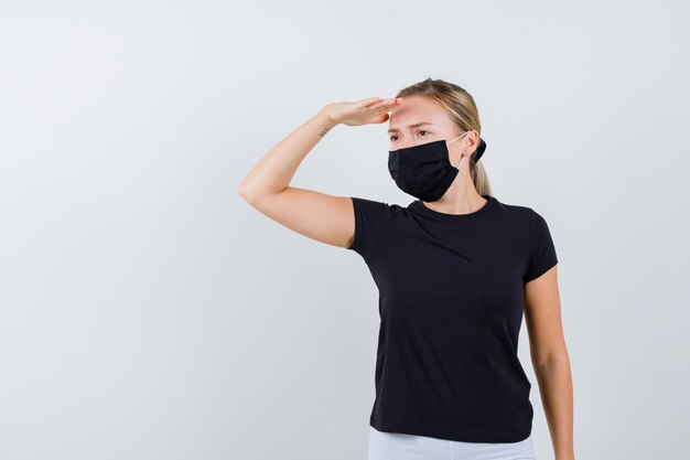 Blonde woman looking far away with hand over head in black t-shirt, white pants