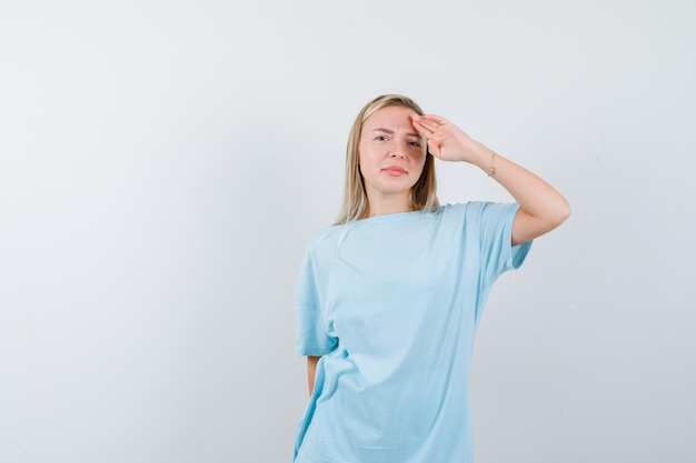 Blonde woman looking far away with hand over head in blue t-shirt and looking cute