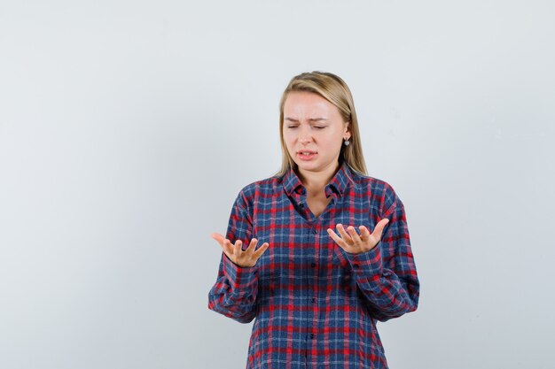 Blonde woman looking at hands surprisingly in checked shirt and looking surprised , front view.