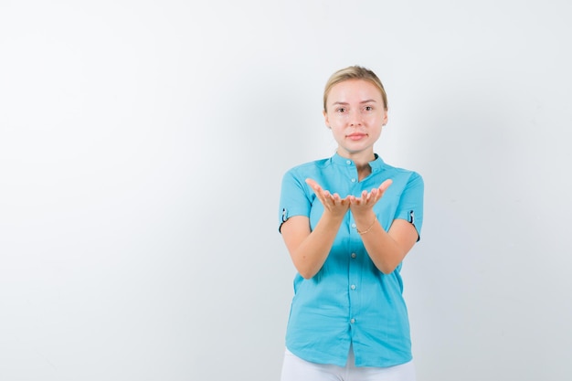 Free photo blonde woman making giving or receiving gesture in blue blouse and looking gentle