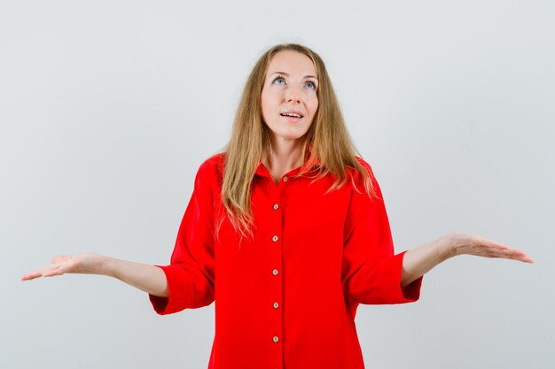 Blonde woman making scales gesture in red shirt and looking hopeful.