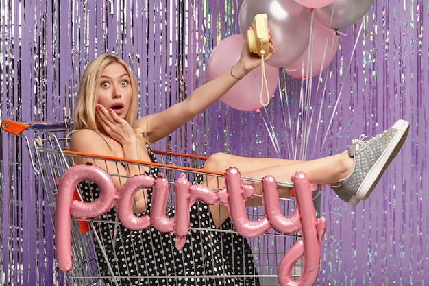 Free photo blonde woman at party in shopping cart holding balloons