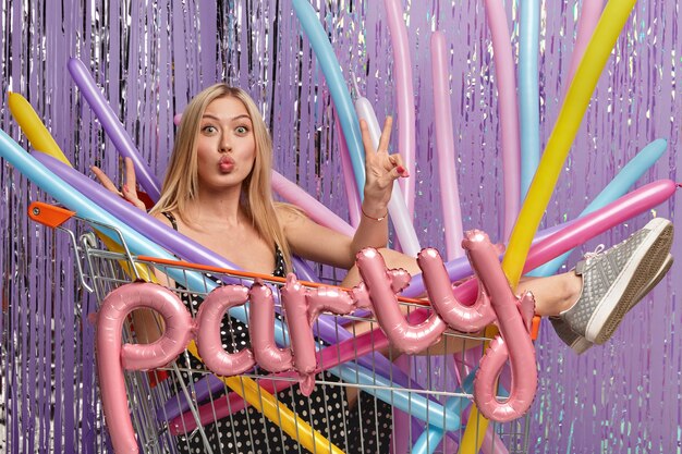 Blonde woman at party in shopping cart holding balloons