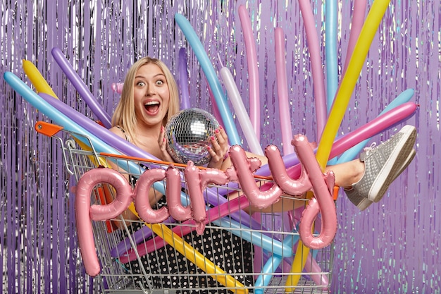 Blonde woman at party in shopping cart holding balloons