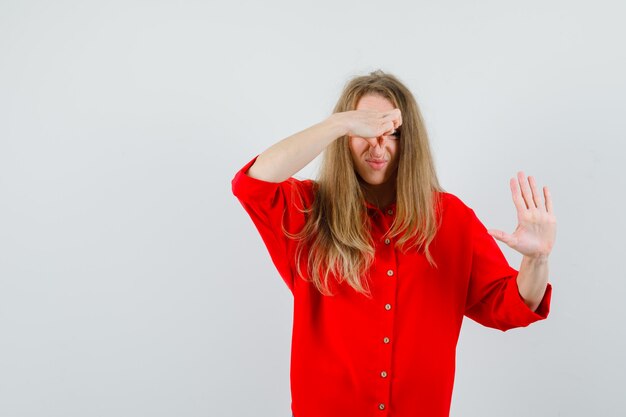 Blonde woman pinching nose due to bad smell in red shirt and looking disgusted.