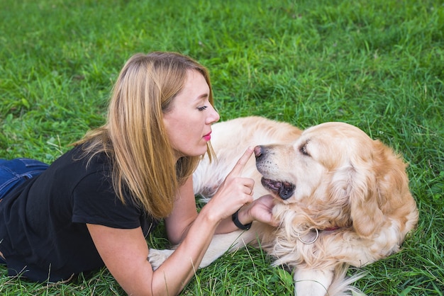 Blonde woman playing with dog retriever touching the dog's nose. fun game on the grass in the park