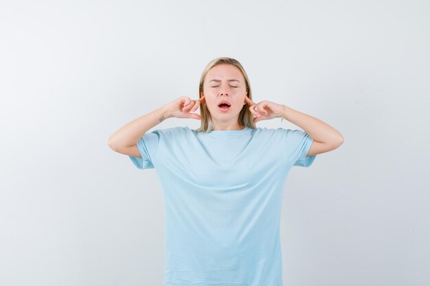 Blonde woman plugging ears with index fingers, keeping mouth wide open