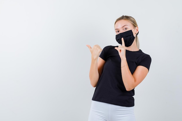 Free photo blonde woman pointing aside with thumb, showing silence gesture in black t-shirt