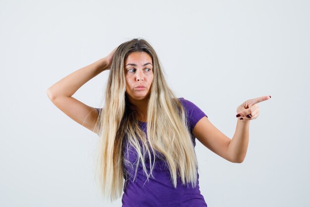 blonde woman pointing away in violet t-shirt and looking curious. front view.