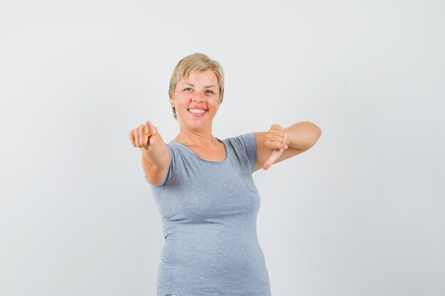 Blonde woman pointing down in light blue t-shirt and looking happy , front view.