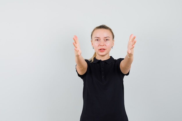 Blonde woman pointing at front with both hands in black t-shirt and looking optimistic