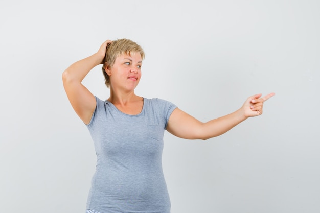 Blonde woman pointing to the right side with index fingers in light blue t-shirt and looking pensive. front view.