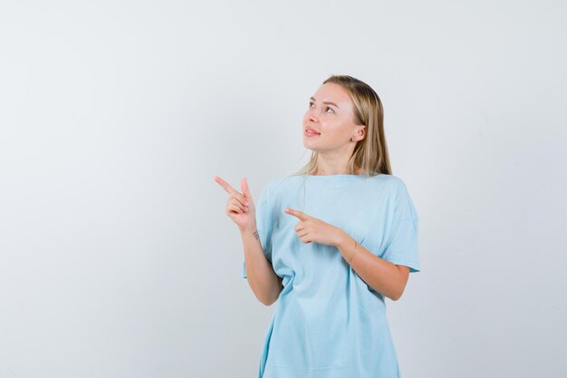 Blonde woman pointing right with index fingers in blue t-shirt and looking cute