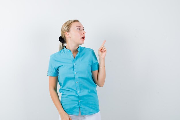 Blonde woman pointing up in blue blouse and looking amazed isolated