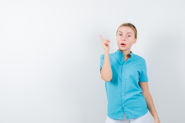 Blonde woman pointing up in blue blouse and looking puzzled