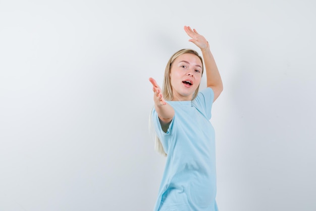 Blonde woman pointing with index fingers in blue t-shirt and looking happy