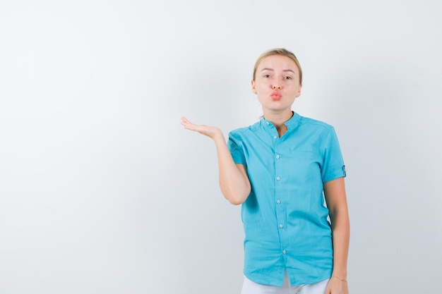 Blonde woman pouting lips, spreading palm aside in blue blouse isolated