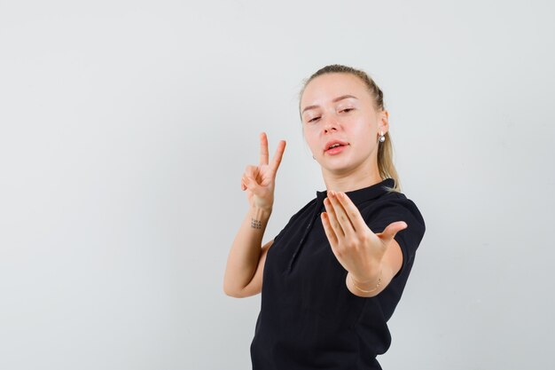 Blonde woman pretending like taking selfie and showing peace sign in black t-shirt