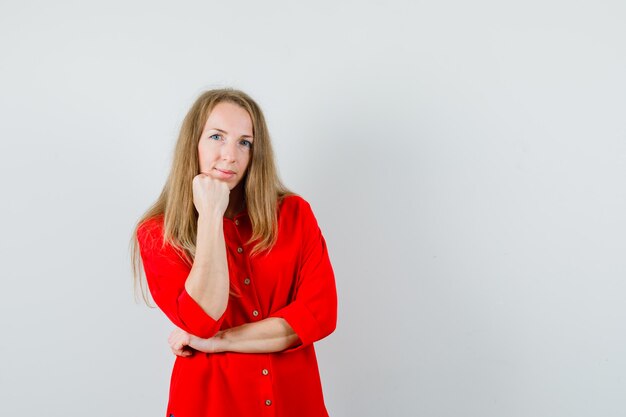 Blonde woman propping chin on fist in red shirt and looking sensible.