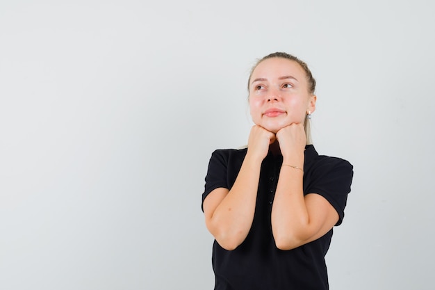 Donna bionda che mette le mani sotto il mento in maglietta nera