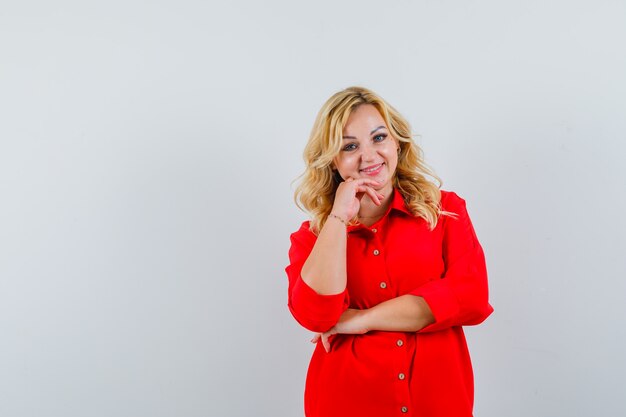 Blonde woman in red blouse leaning cheek on hand and looking happy