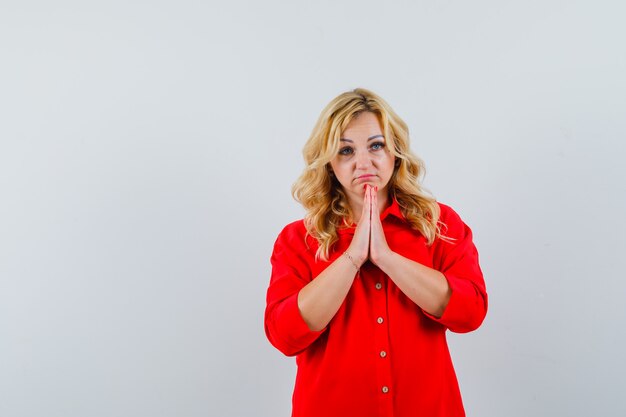 Blonde woman in red blouse standing in prayer pose and looking focused