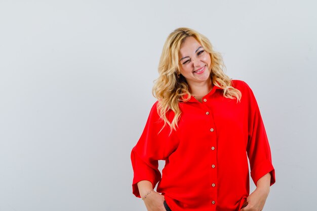 Blonde woman in red blouse standing straight and posing at camera and looking happy