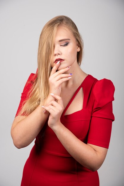 Blonde woman in red outfit touching her mouth.