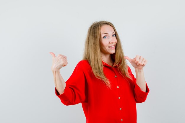 Blonde woman in red shirt pointing back with thumbs and looking joyful ,