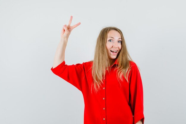Blonde woman in red shirt showing victory gesture and looking happy ,