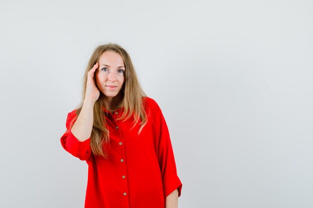 Blonde woman in red shirt touching face skin on cheek and looking attractive ,