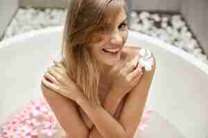 Foto gratuita donna bionda rilassante nella vasca da bagno con petali